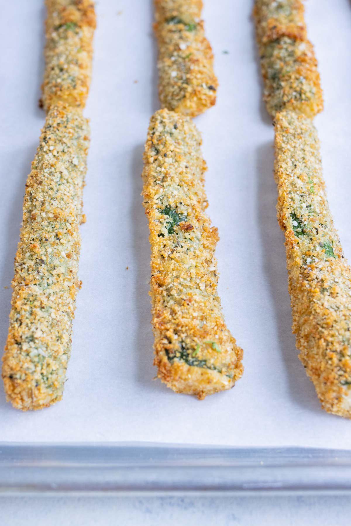 Baked zucchini fries on a baking sheet with parchment paper.