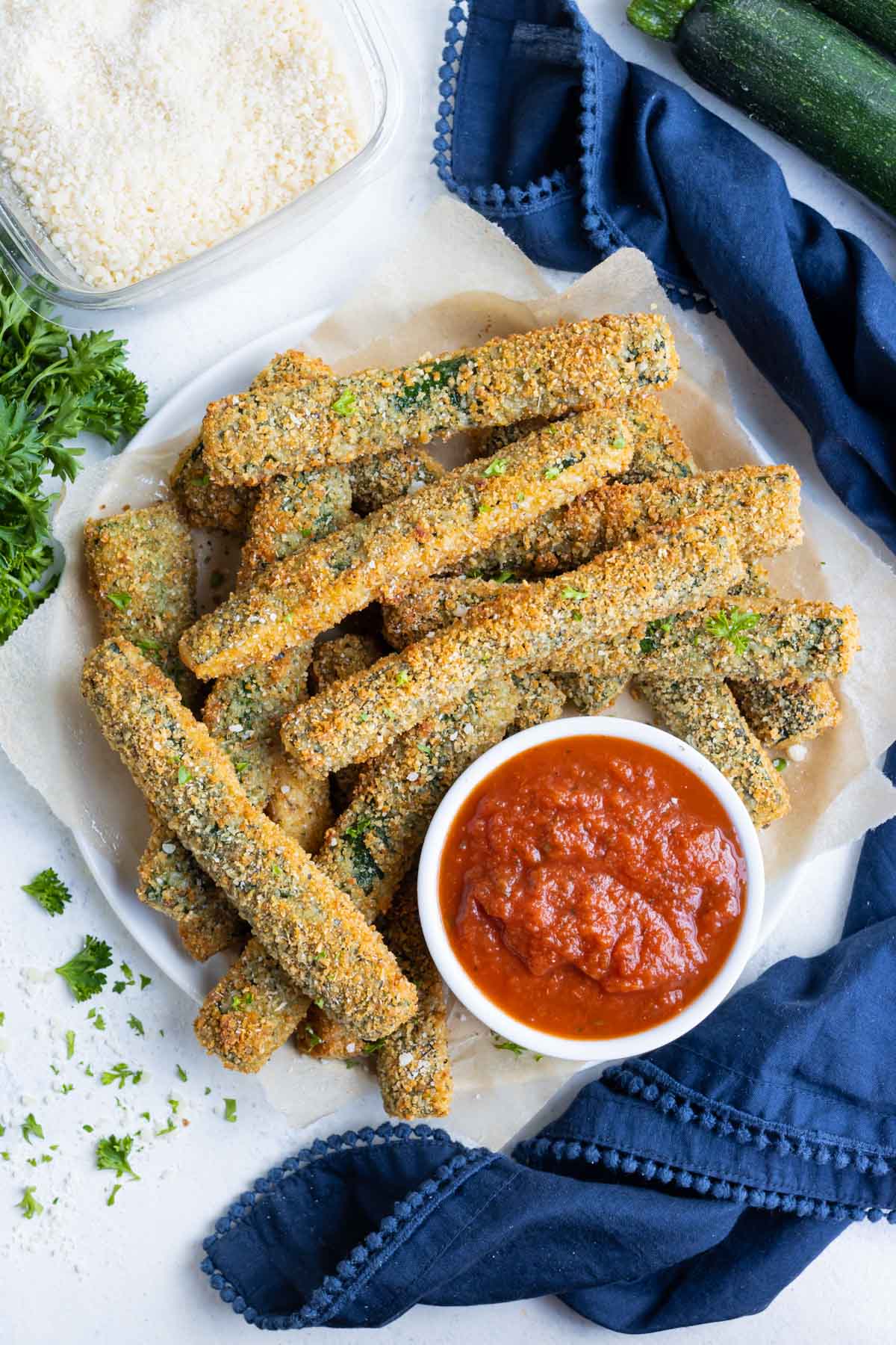 Air fryer zucchini fries on a white plate with a bowl of marinara sauce on the side.