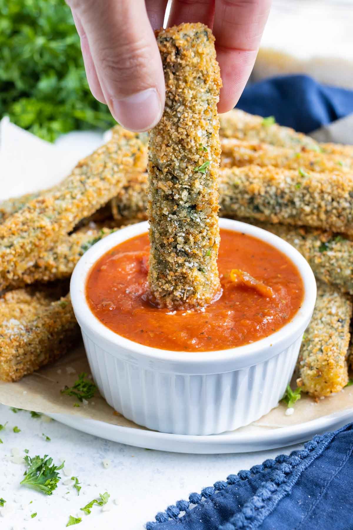 A hand dipping a zucchini fry into marinara sauce.