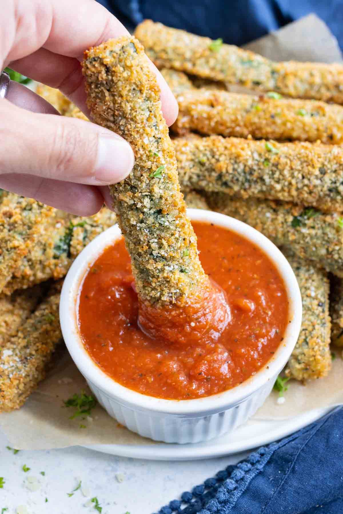 Parmesan zucchini fries dipped in sauce on a white plate.