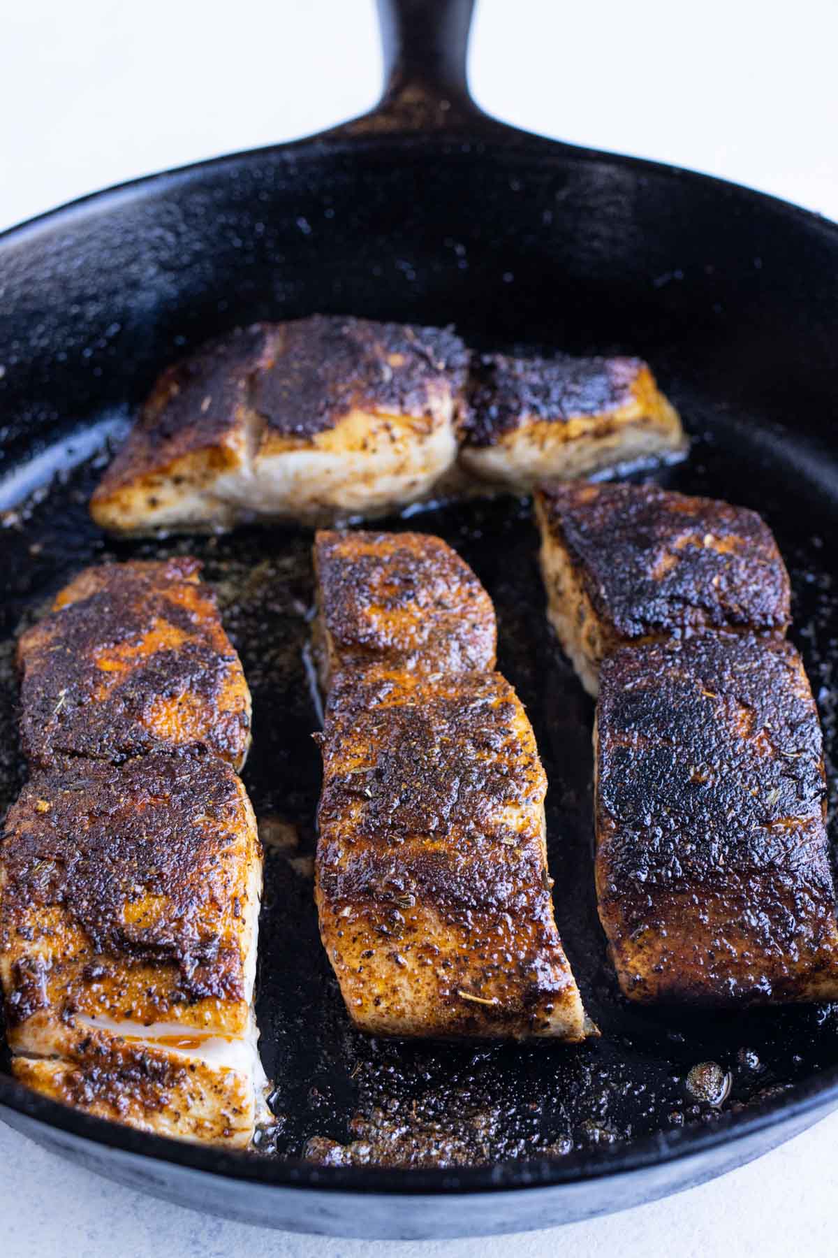 Blackened mahi mahi is flipped over, skin side-down, and continues to cook in a cast-iron skillet.