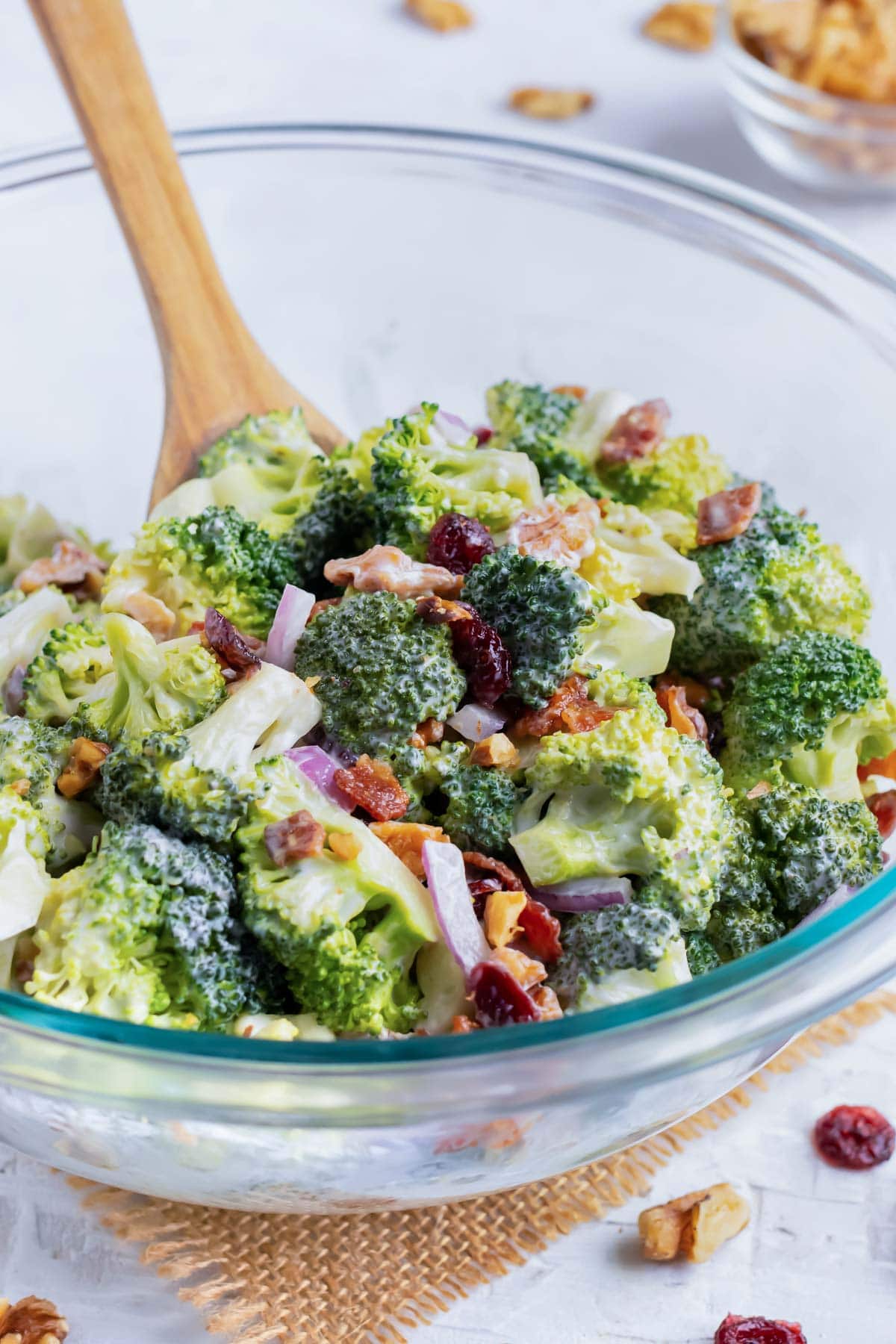 Broccoli Bacon Salad in a clear glass bowl with a wooden spoon stirring it.