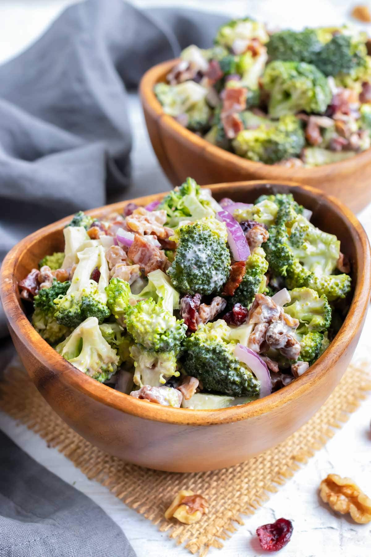 A wooden serving bowl full of a cold broccoli salad recipe with walnuts, cranberries, and bacon.