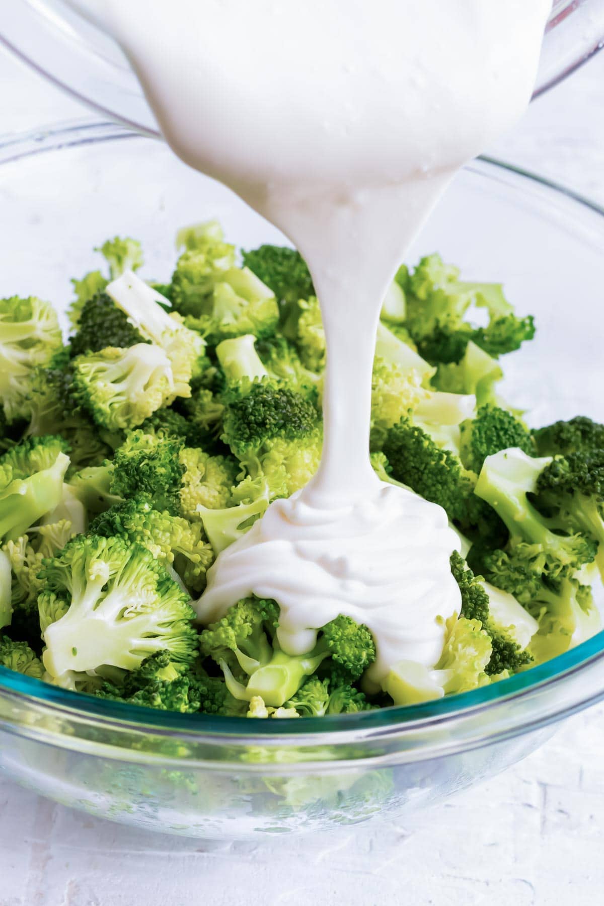 Pouring creamy dressing over cooked broccoli.
