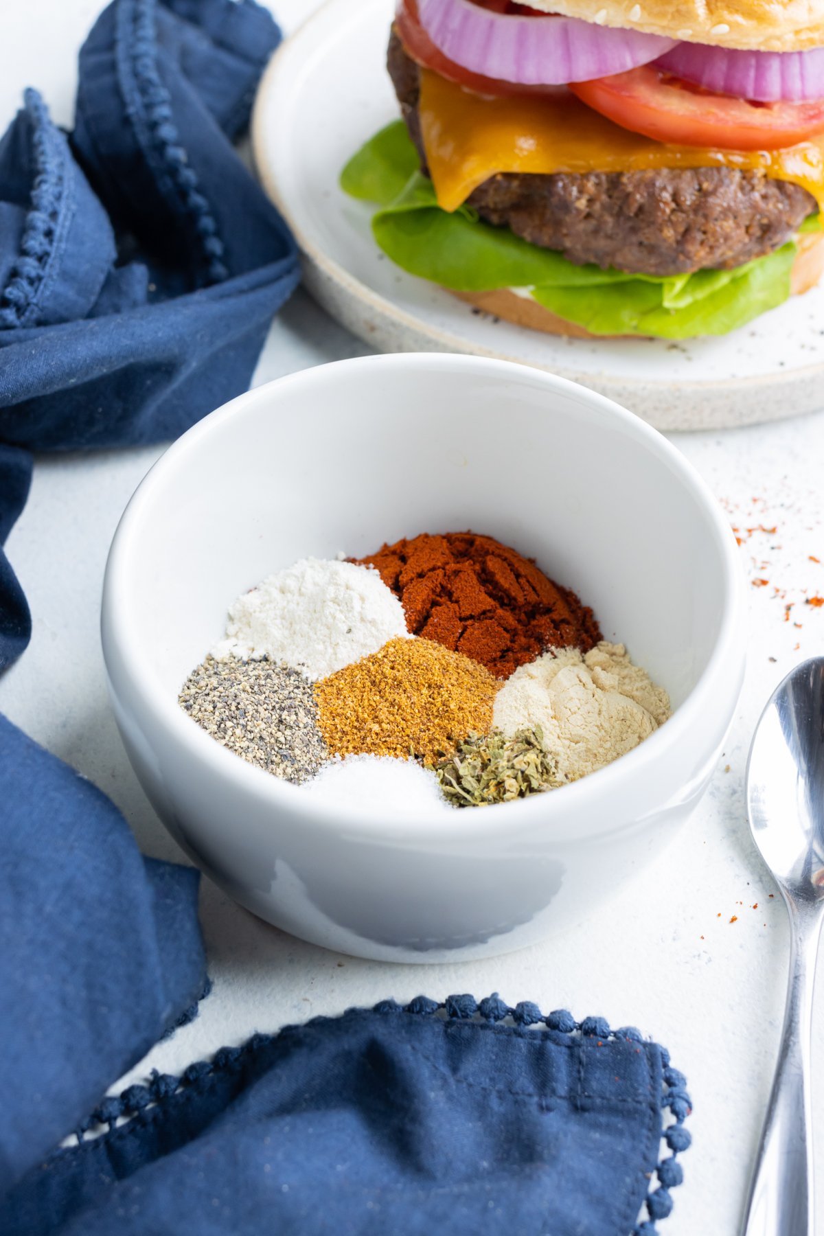 A white bowl is filled with different spices used for burger seasoning.