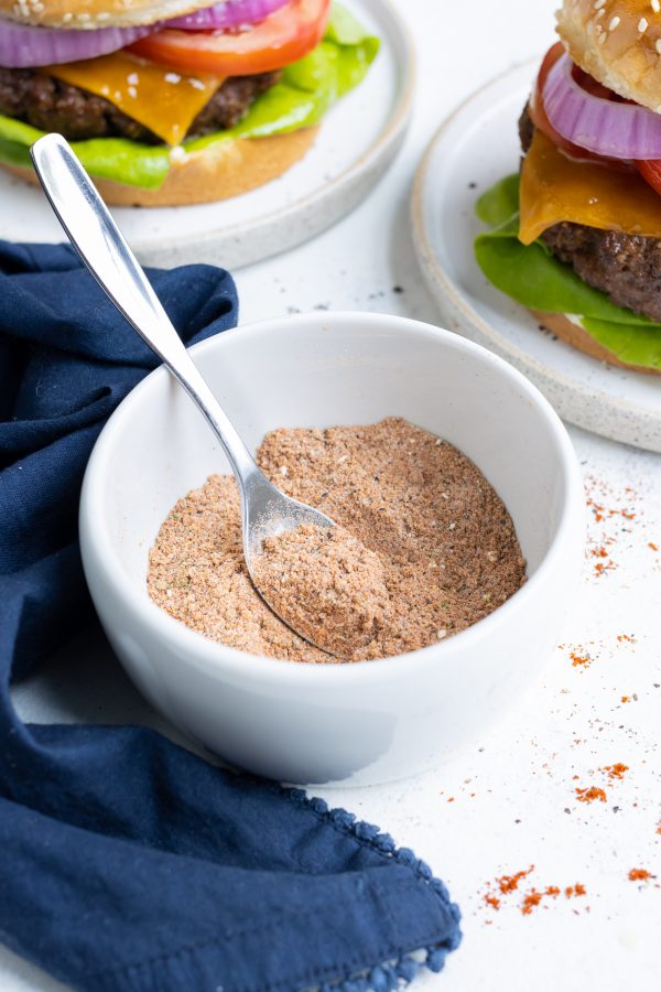 A bowl full of burger seasoning is shown on the counter with a spoon.