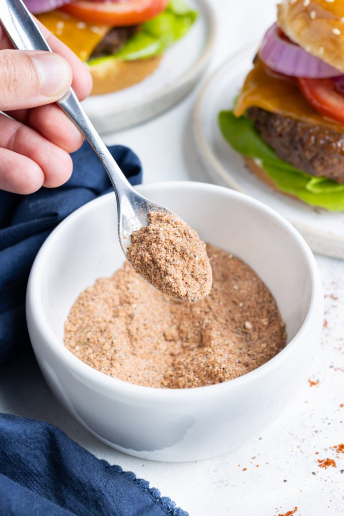 Homemade Burger seasoning is picked up by a spoon before putting on a patty.