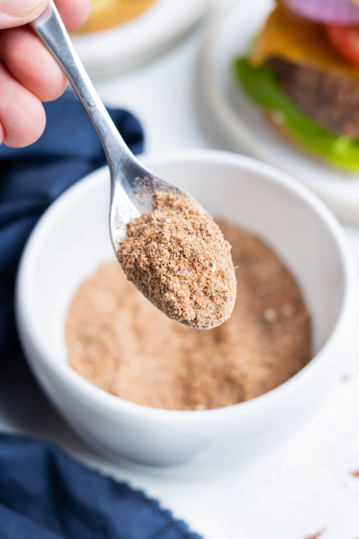 A spoon is shown holding homemade burger seasoning before using.