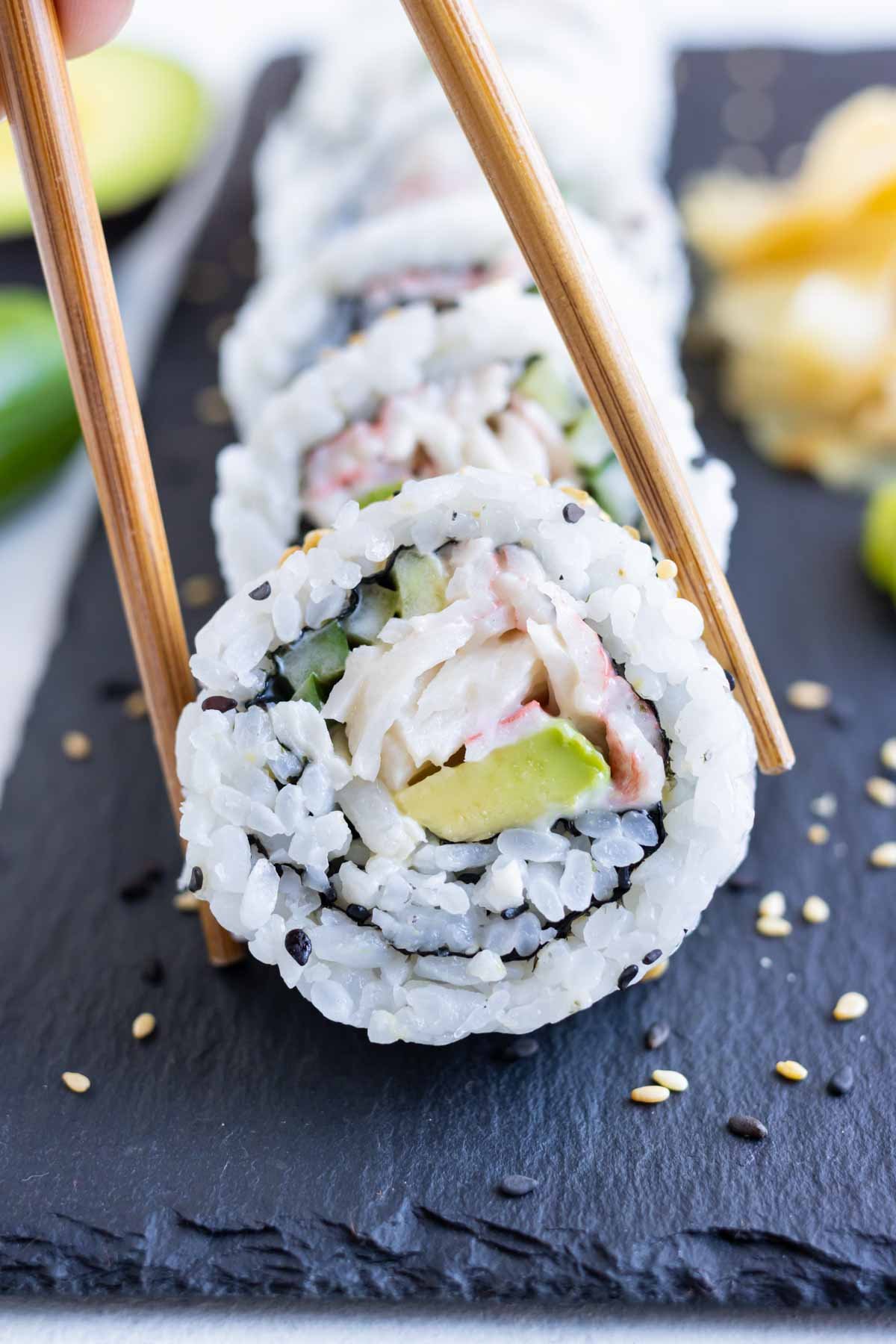 Chopsticks are used to pick up a California sushi roll piece.