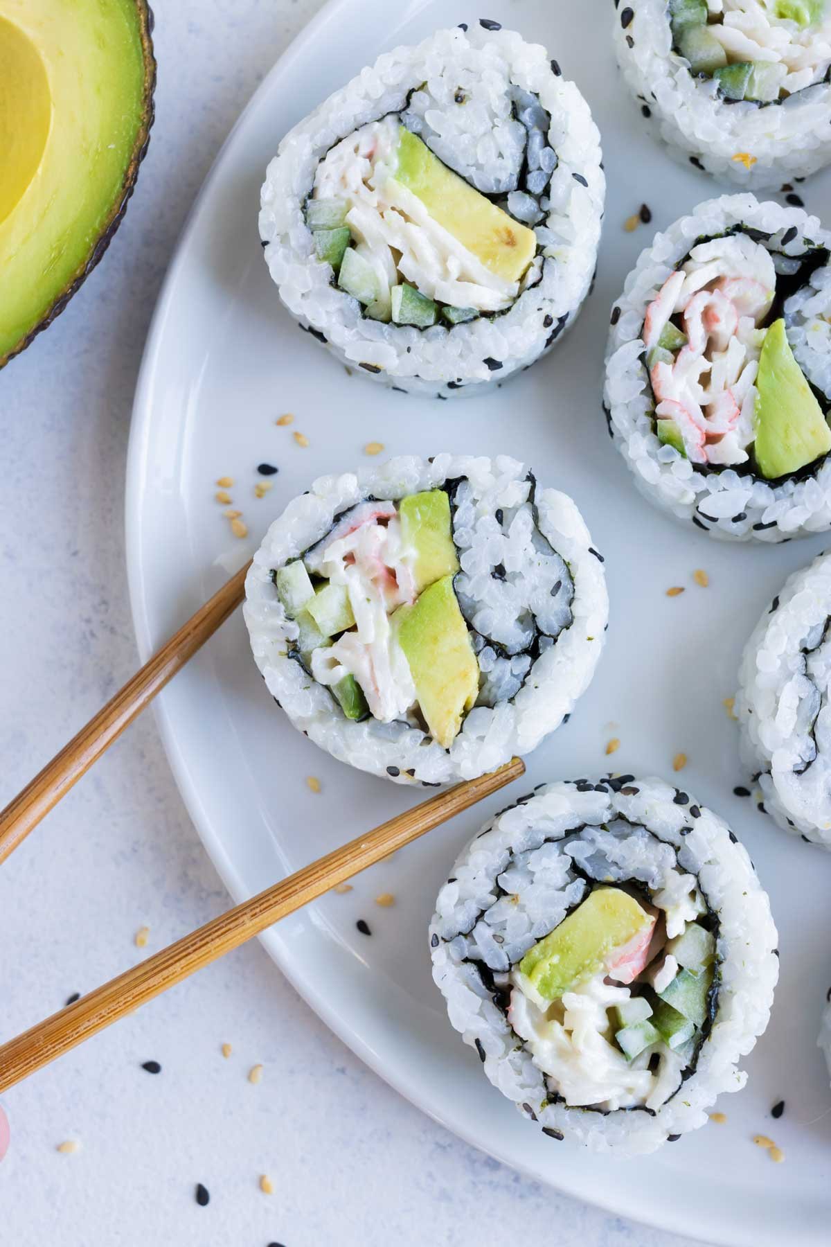 Chopsticks are shown picking up a sushi roll from a plate.