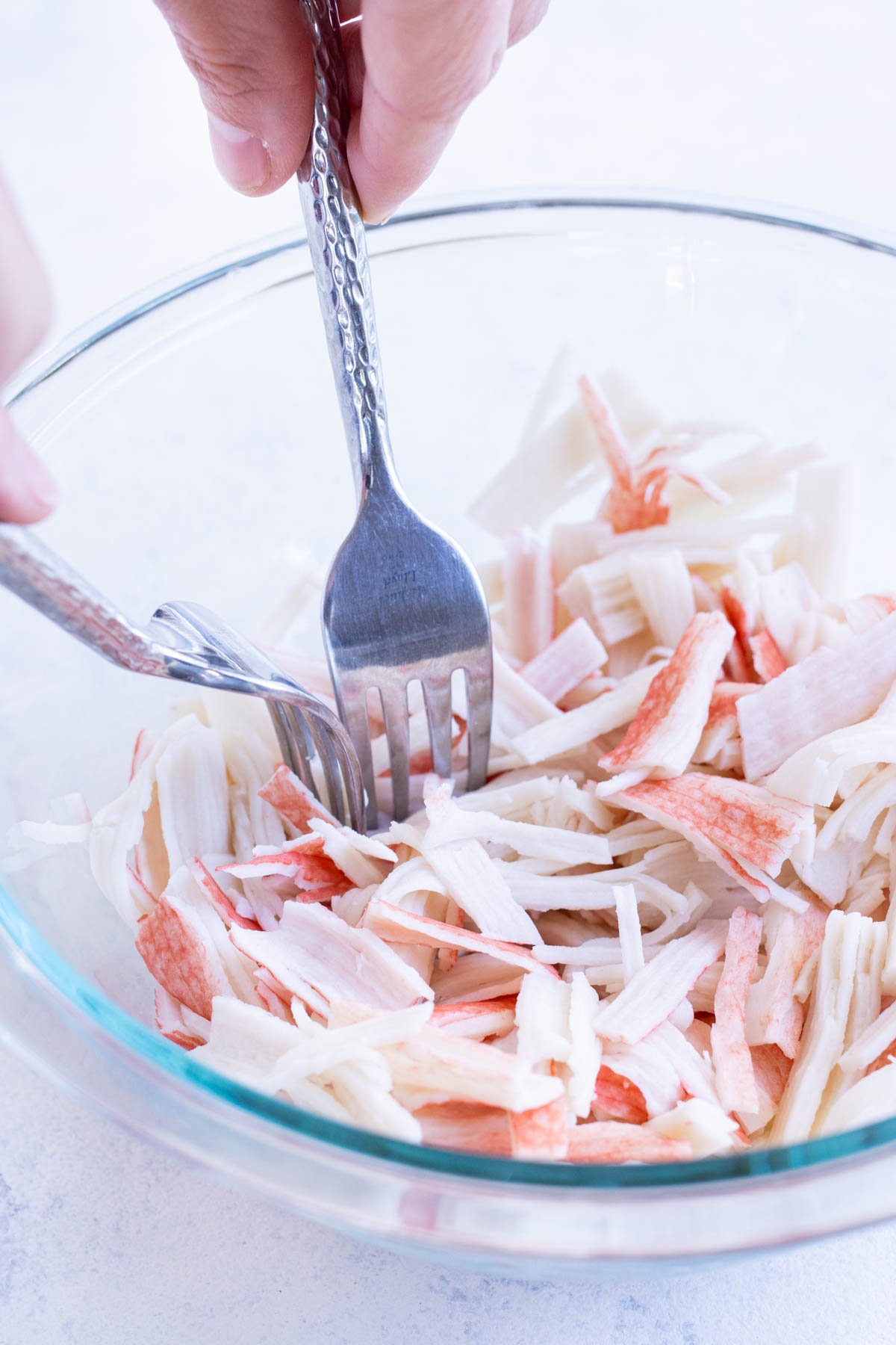 Crab is shredded with two forks in a bowl.