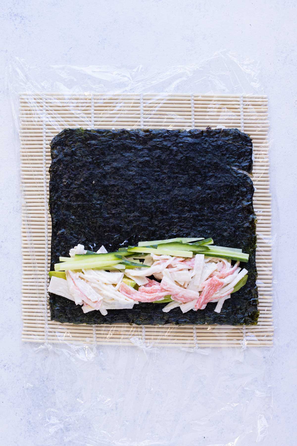 Cut cucumbers and crab are laid on one side of the nori.