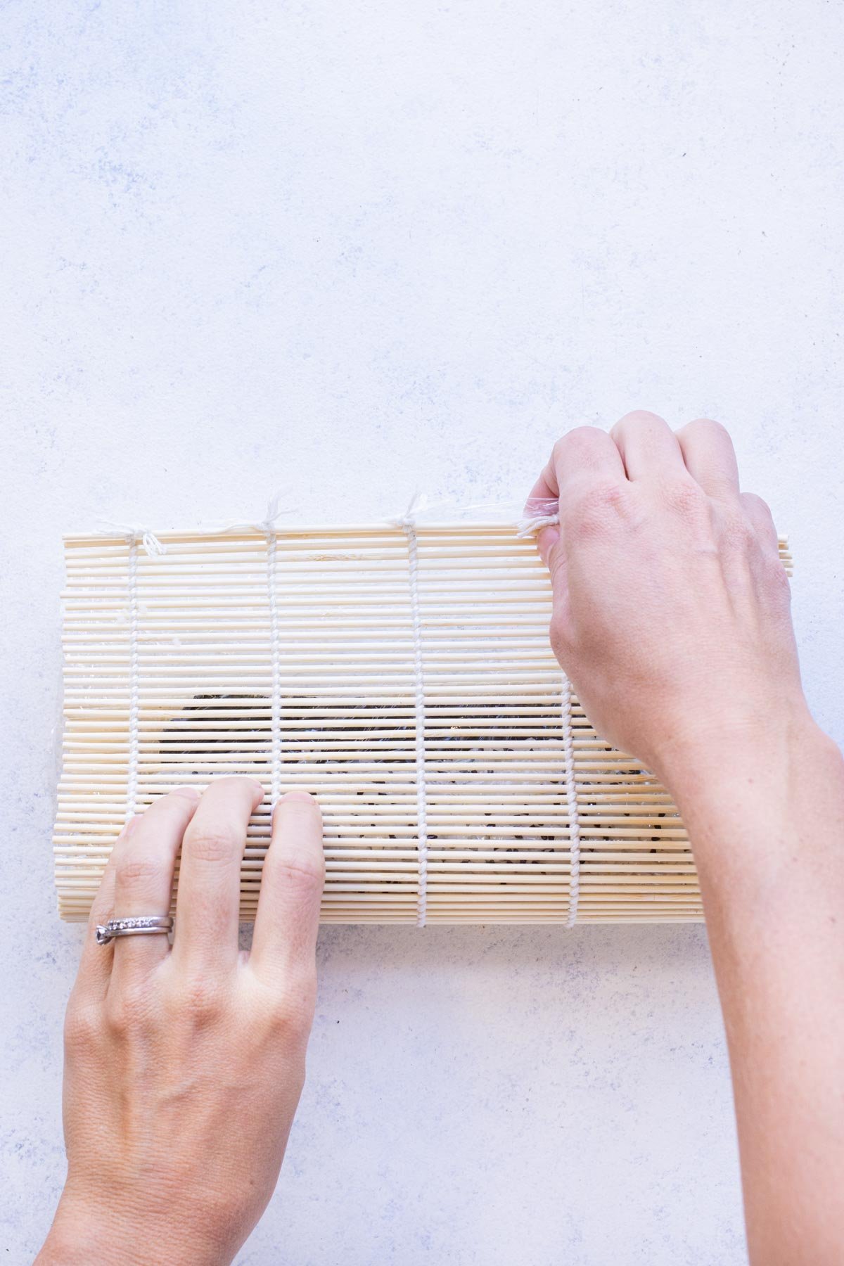 A bamboo mat is used to roll up a California sushi roll.