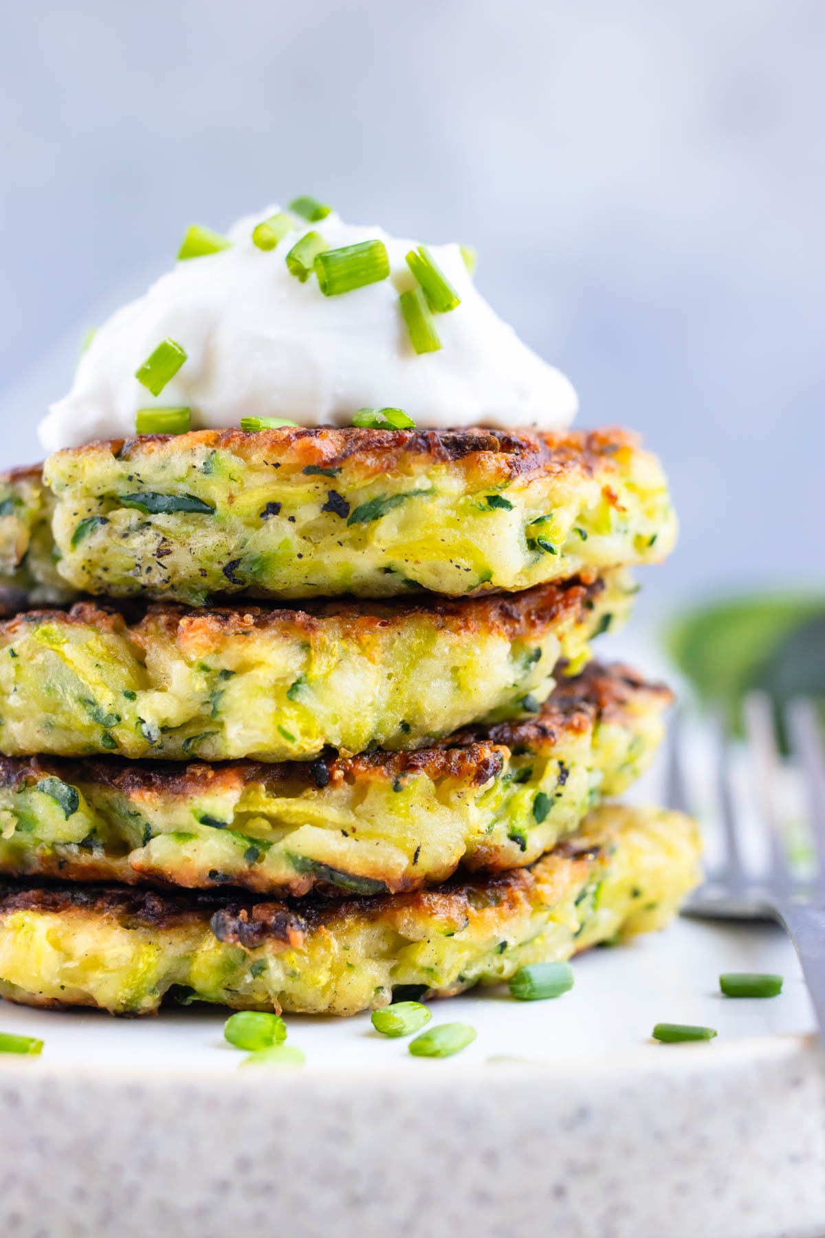Four zucchini fritters in a stack on a white plate.