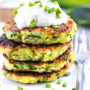 A stack of fried zucchini fritters with sour cream on top.