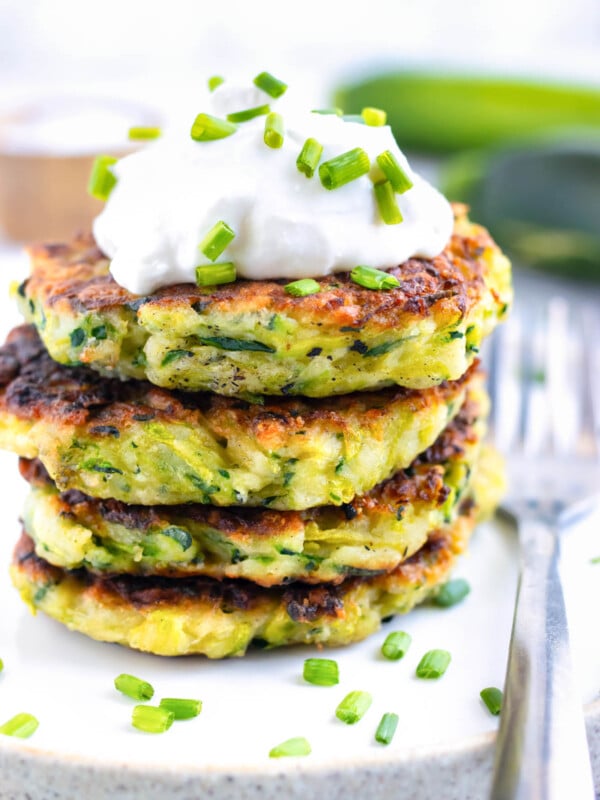 A stack of fried zucchini fritters with sour cream on top.