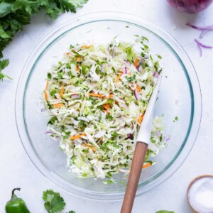 A glass bowl is filled with cabbage and other ingredients for this taco slaw.