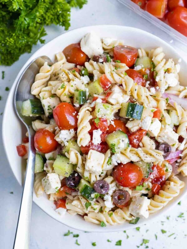 A simple Greek pasta salad is served in a white bowl with a spoon.