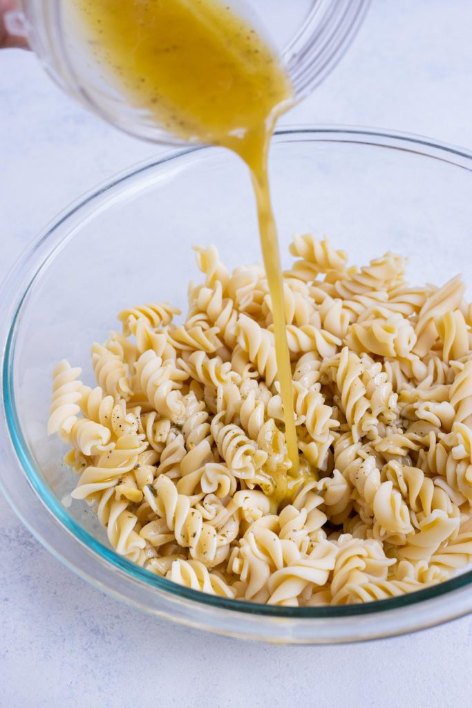 Greek dressing is poured over pasta in a bowl.