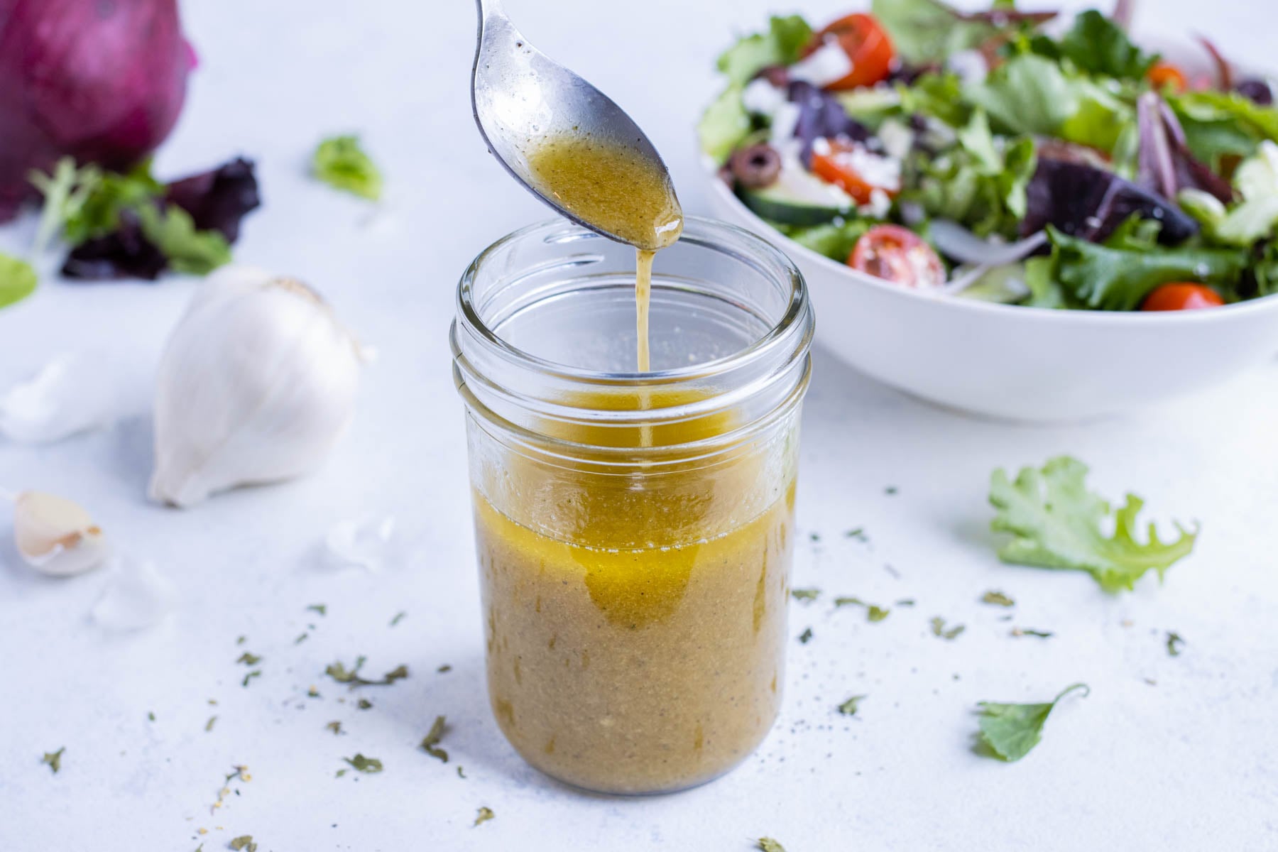 Greek salad dressing is picked up with a spoon to be served over a cucumber tomato salad.