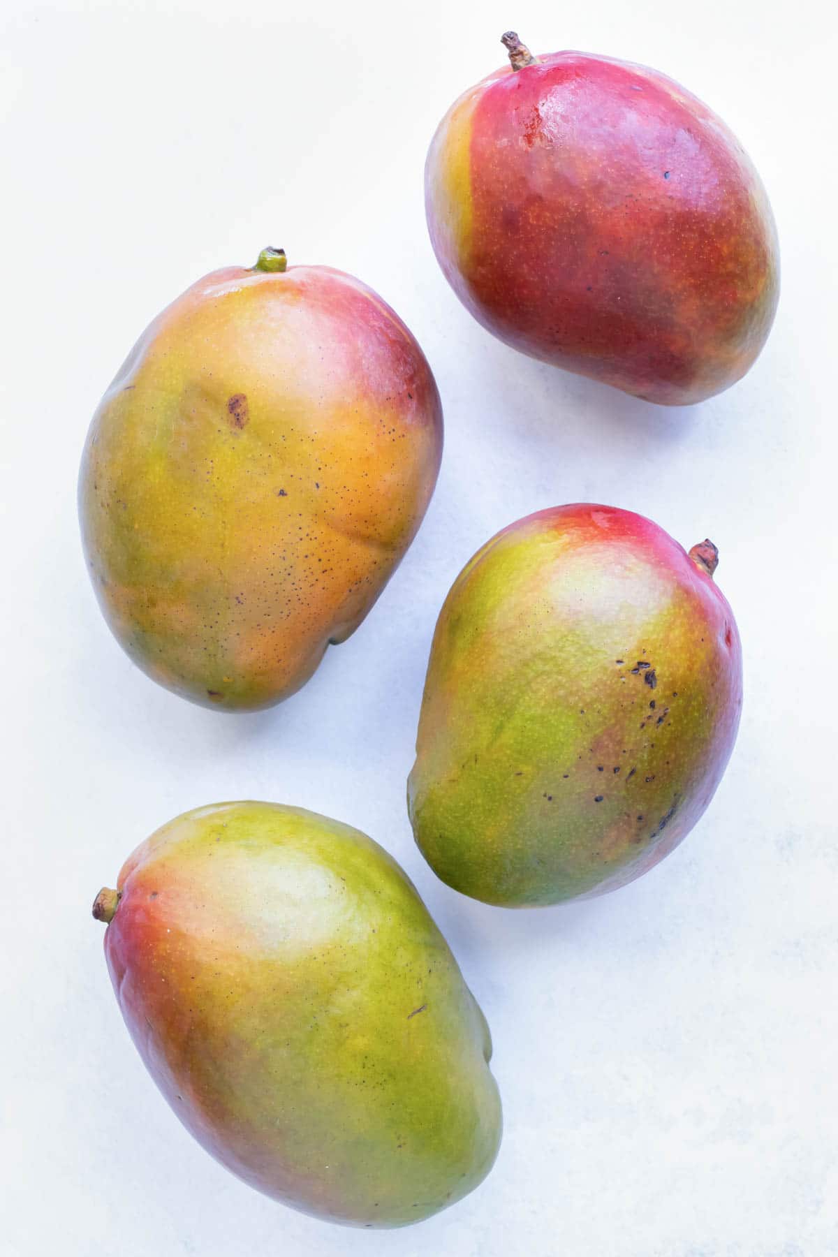 Four ripened mangos with their stems.