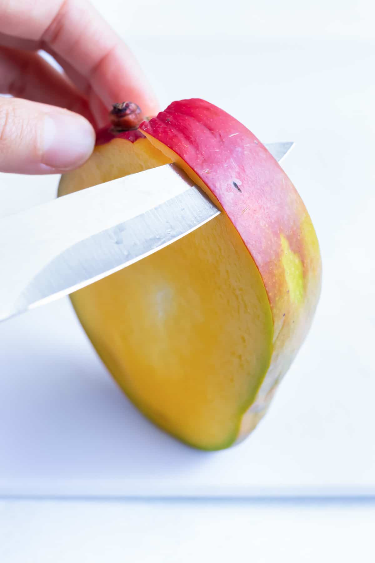 A small knife removes the peel from a wedge of mango.