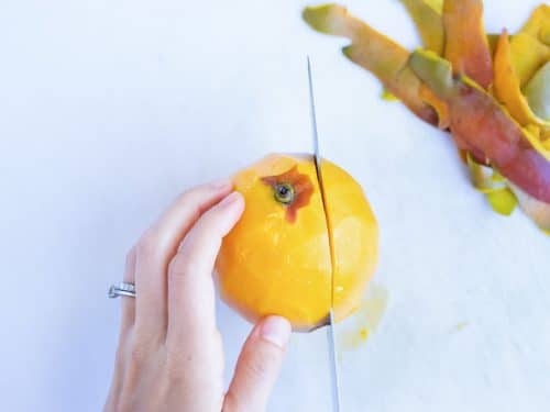 A hand holding a mango firmly while cutting it in half.