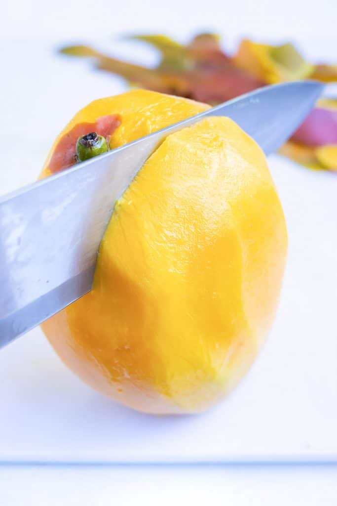 Cutting the edge off of a peeled mango.