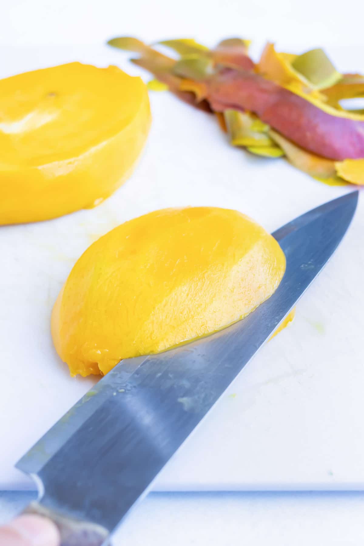 A knife making cuts across the mango while firmly holding it on a cutting board.