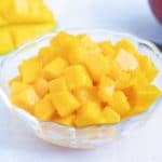 A glass bowl full of cut and diced ripened mango.