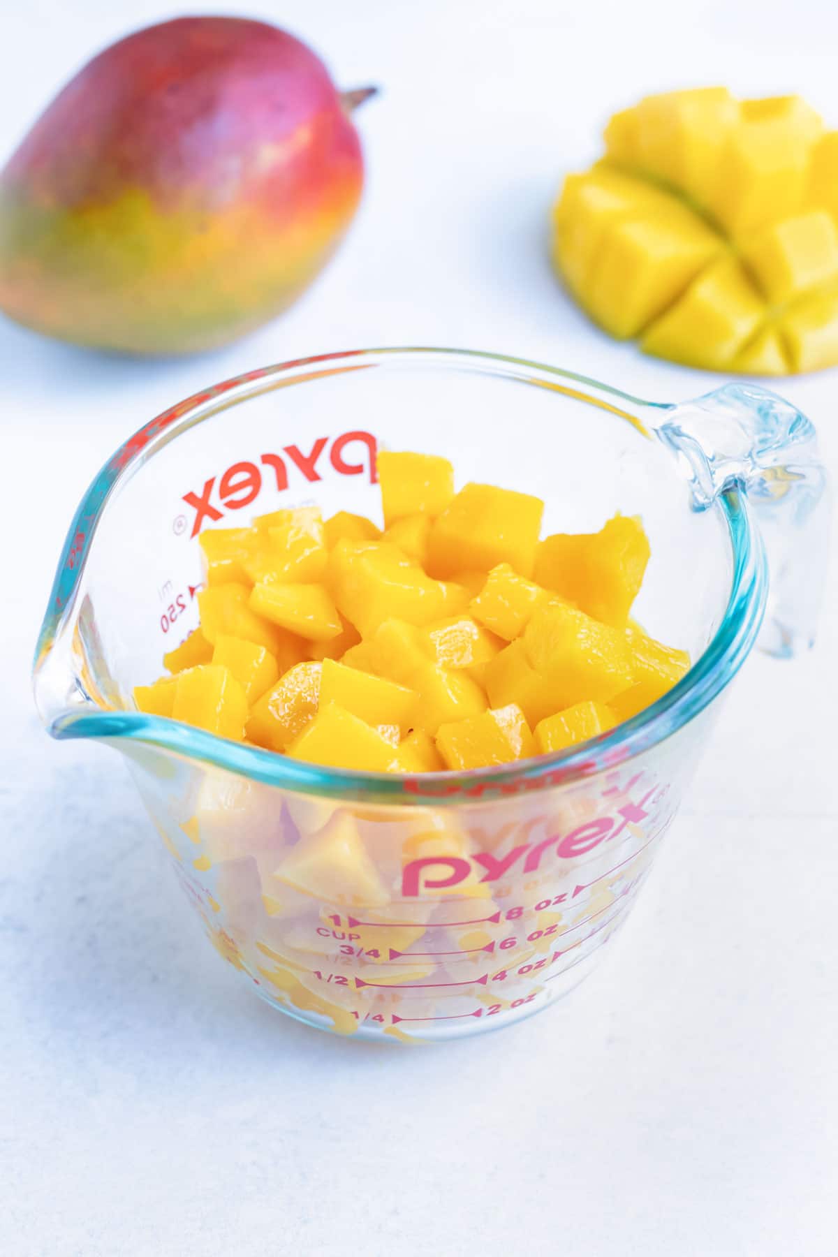 A measuring cup full of freshly cut mango showing that one medium mango equals roughly 1 1/2 cups of fruit.