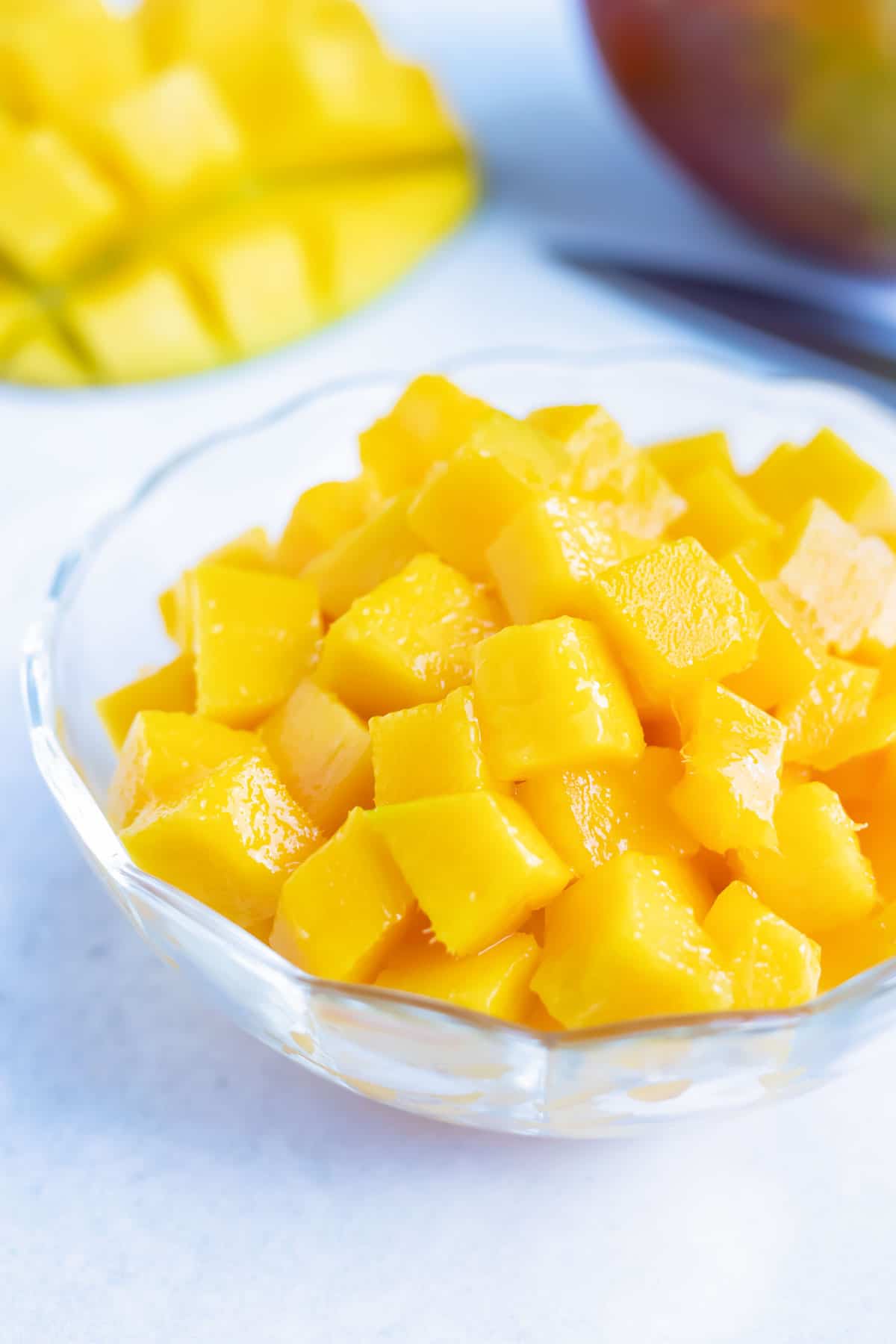 A glass bowl full of cut and diced ripened mango.
