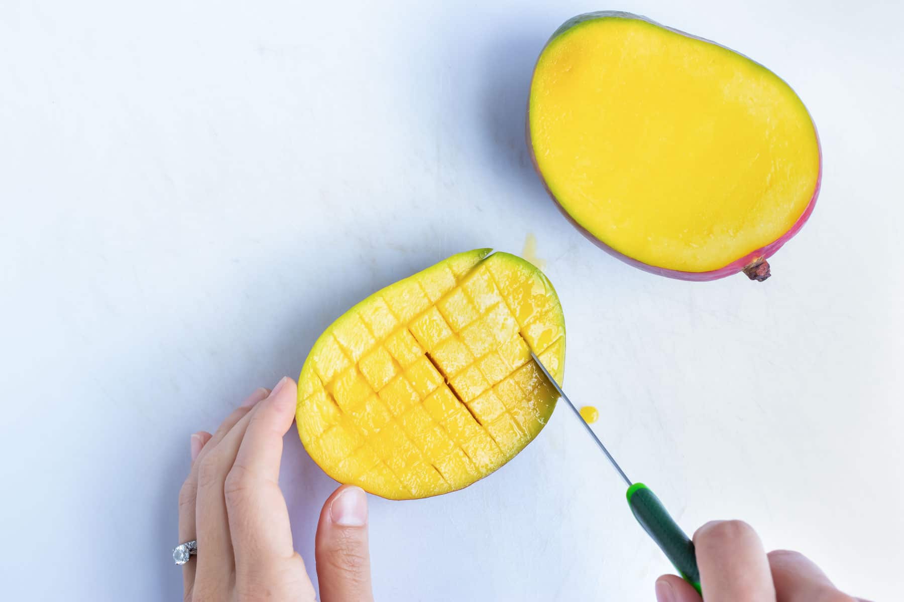 Making horizontal cuts into a mango flesh with a paring knife to dice it.