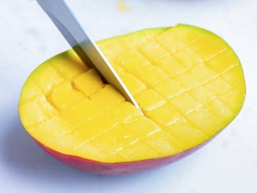 Making cuts into a mango flesh with a paring knife to create a grid.