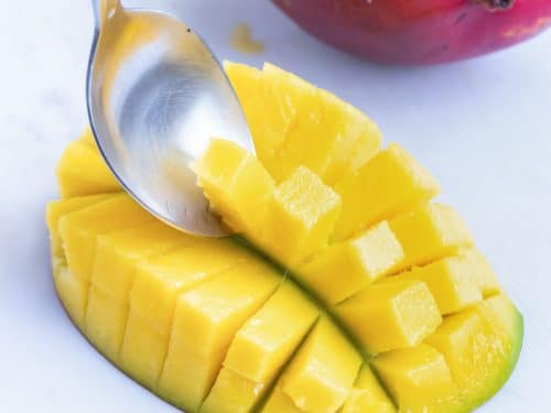 Scooping out cut mango with a spoon to remove the fruit.