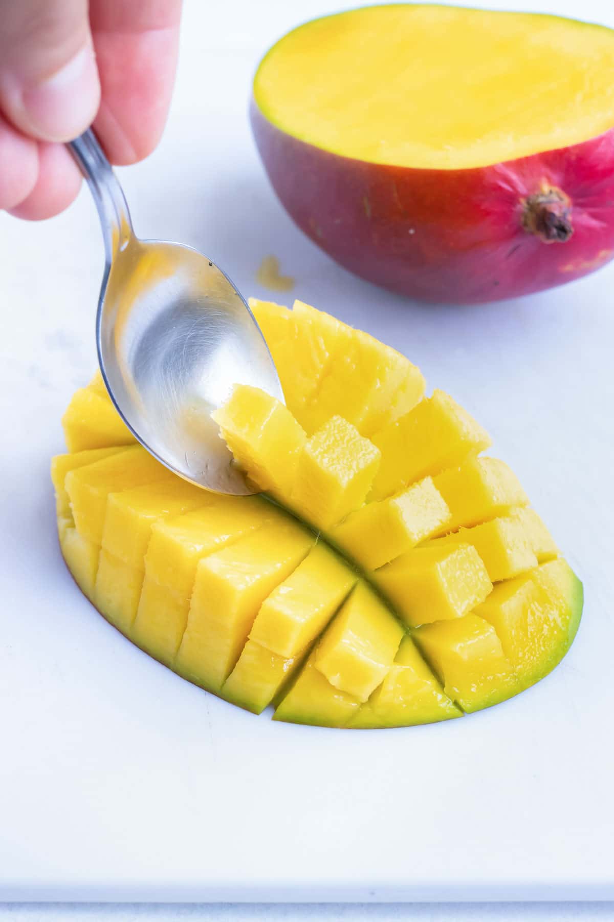 Scooping out cut mango with a spoon to remove the fruit.