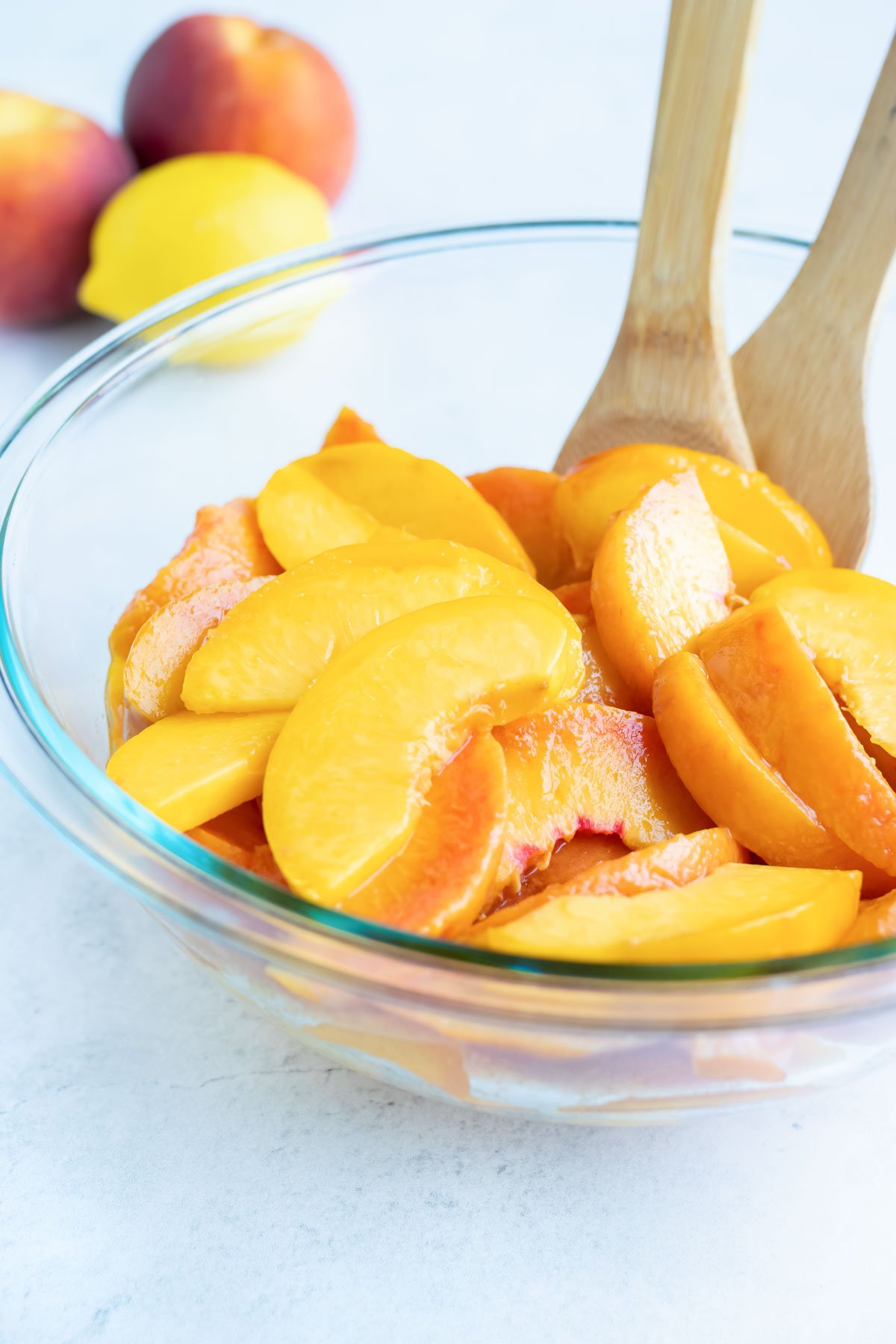 Sliced peaches are placed in a glass bowl as lemon juice is added to prevent browning.