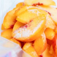 Frozen peaches are shown stacked in a freezer-safe gallon sized plastic bag.