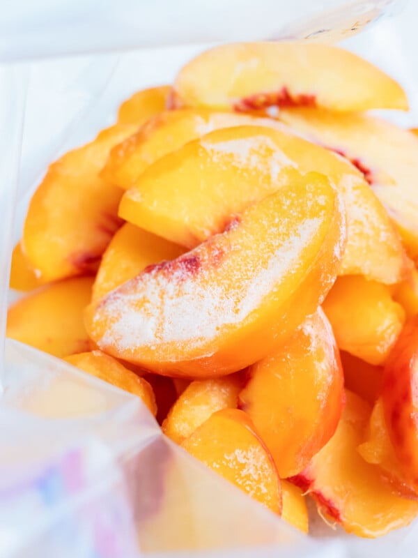 Frozen peaches are shown stacked in a freezer-safe gallon sized plastic bag.