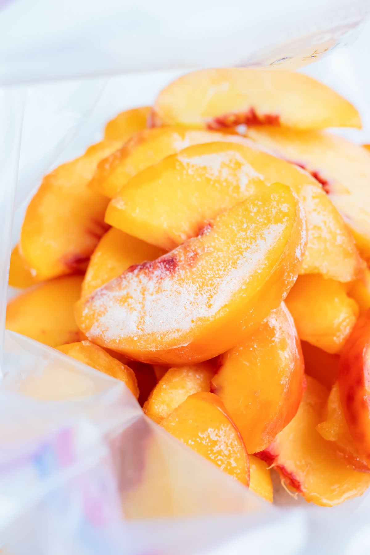 Frozen peaches are shown stacked in a freezer-safe gallon sized plastic bag.