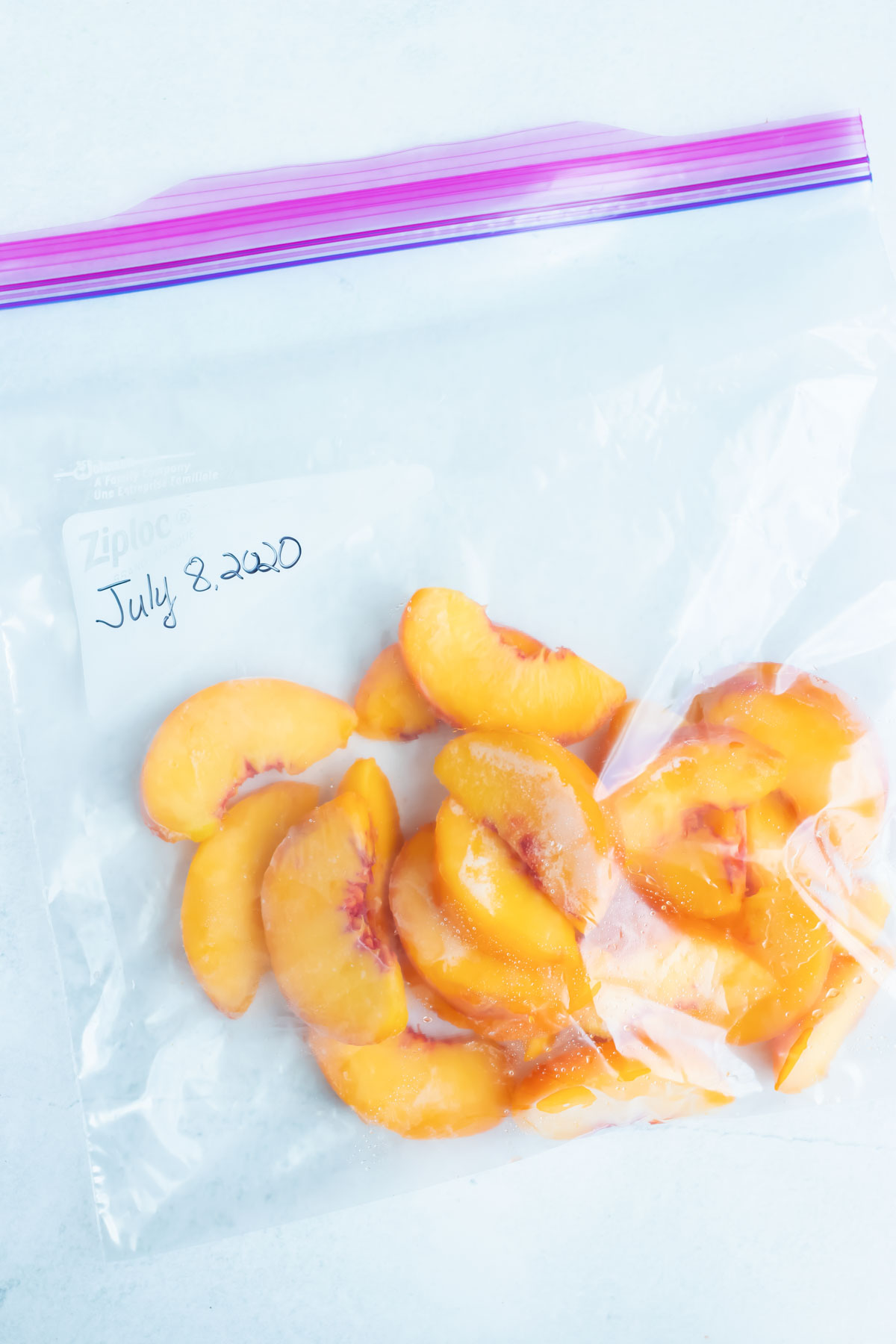 A closed ziplock bag filled with frozen peaches is laying flat on the counter.