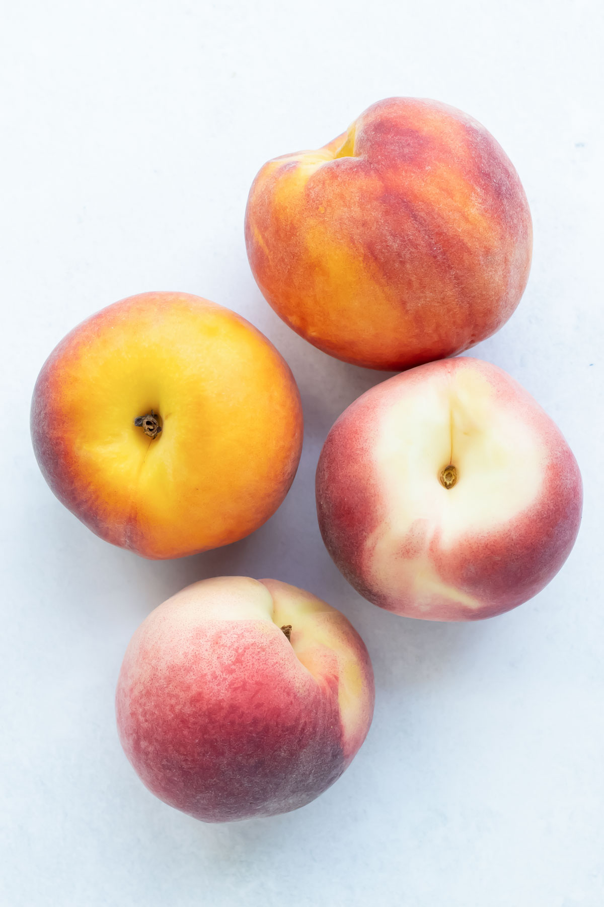 Four ripe peaches are sitting on a white countertop.