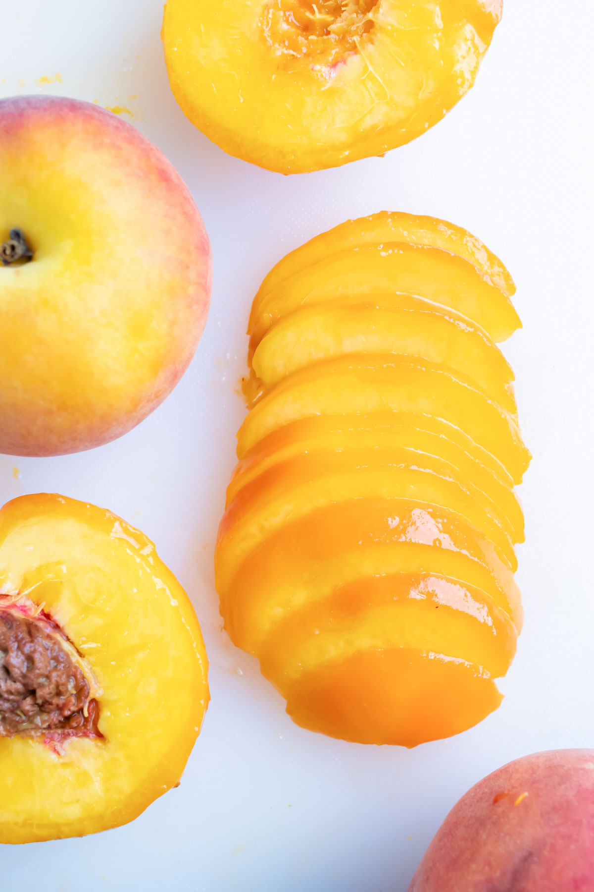 Peaches sit on the counter in various stages of being sliced.