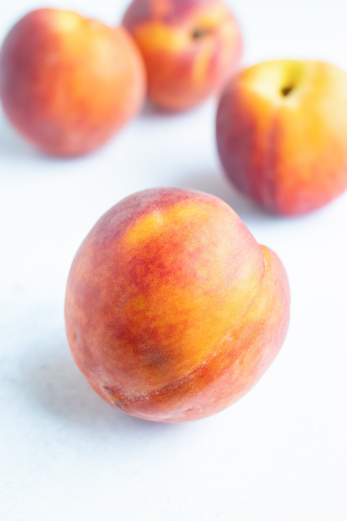 A couple whole peaches are resting on a white counter.