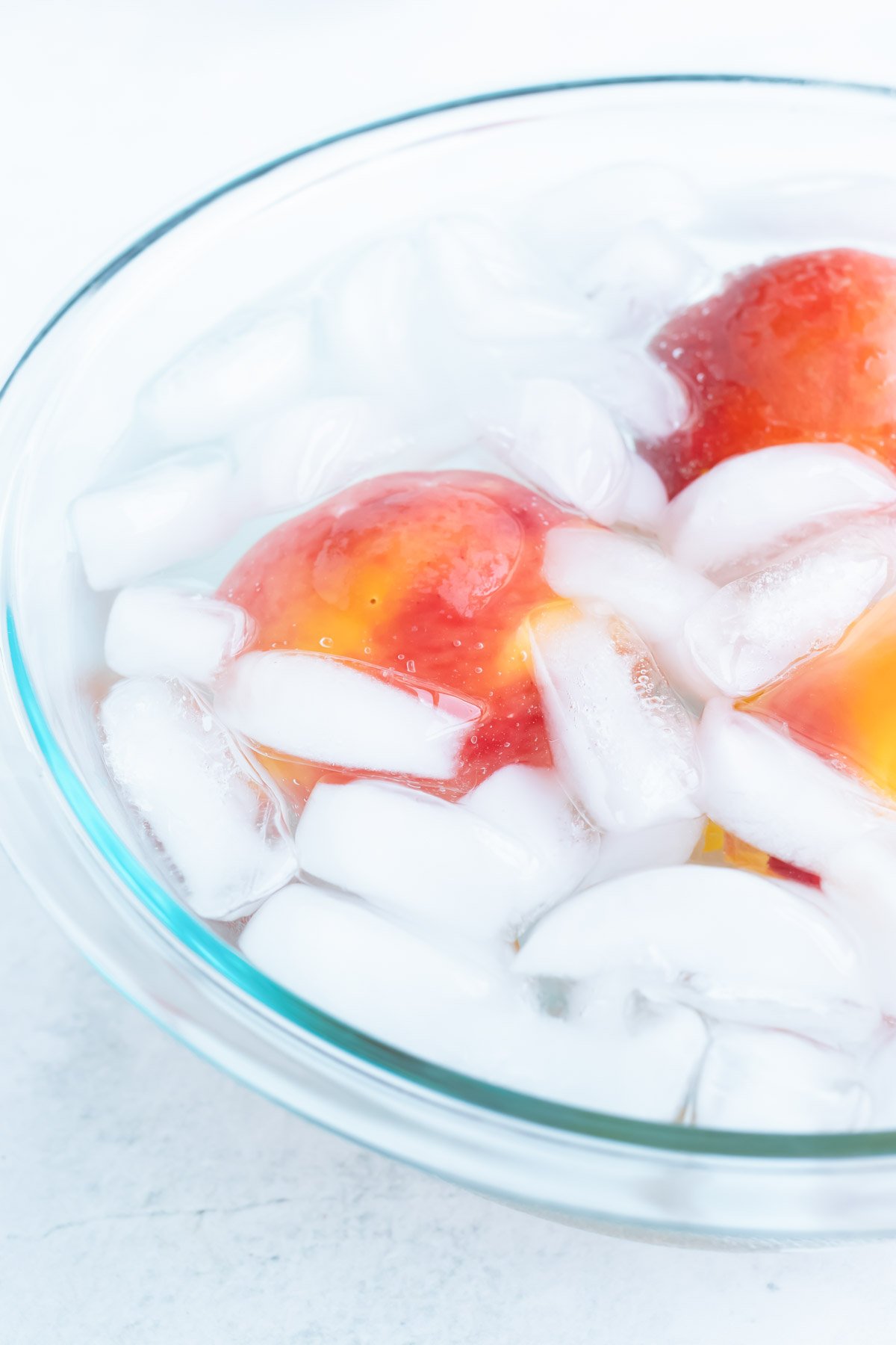 Whole cooked peaches are immediately shocked in a bowl of ice water to stop the cooking process.