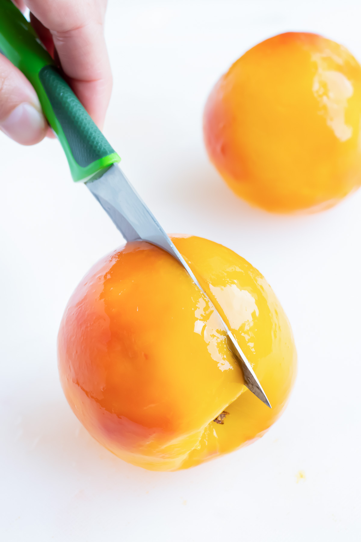 Using a paring knife, slice the fruit in half after it is peeled.