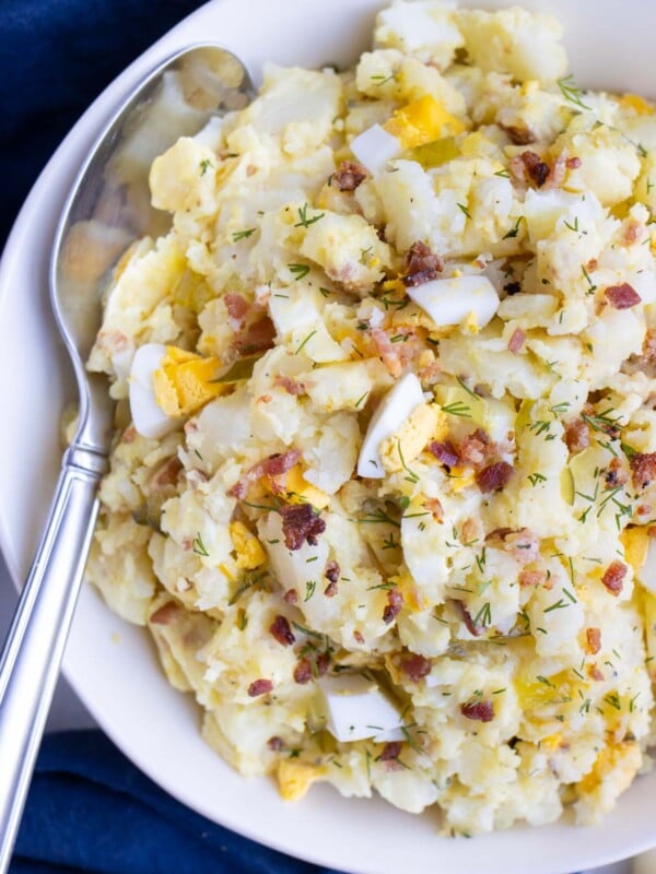 Instant Pot potato salad with bacon and eggs is served from a white bowl with a spoon.