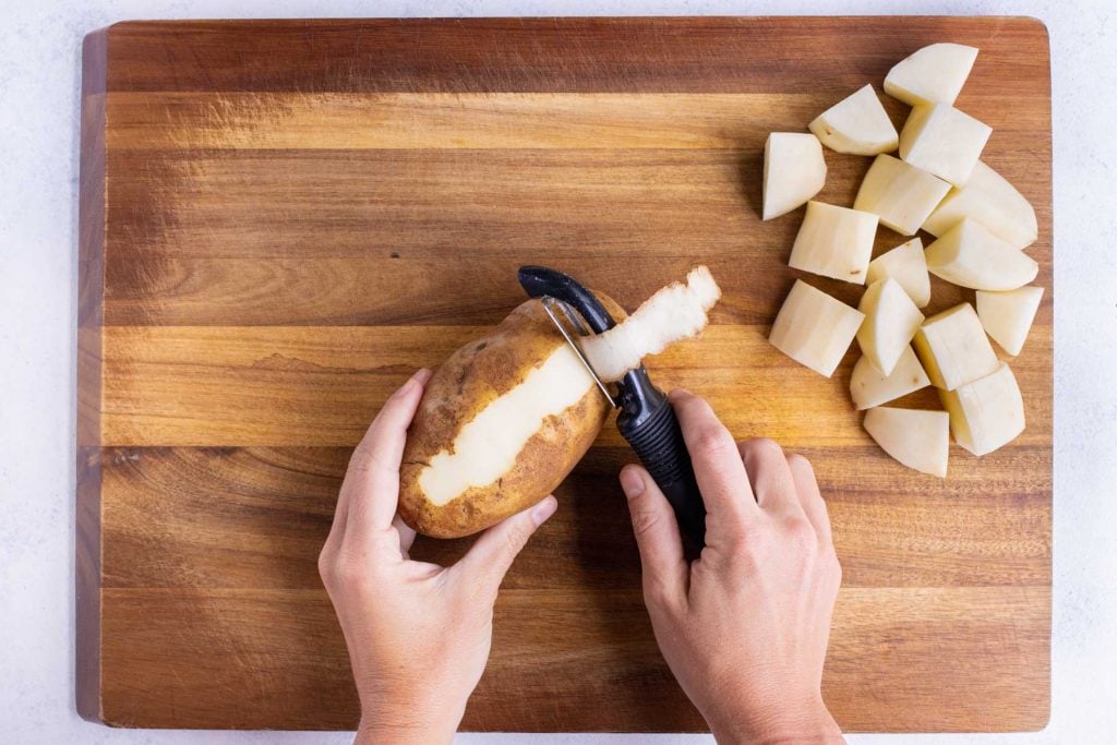 Russet potatoes being peeled with a vegetable peeler for Instant Pot potato salad.