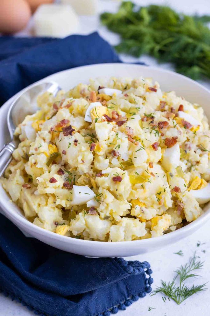 Instant pot potato salad is served at a picnic from a white bowl.