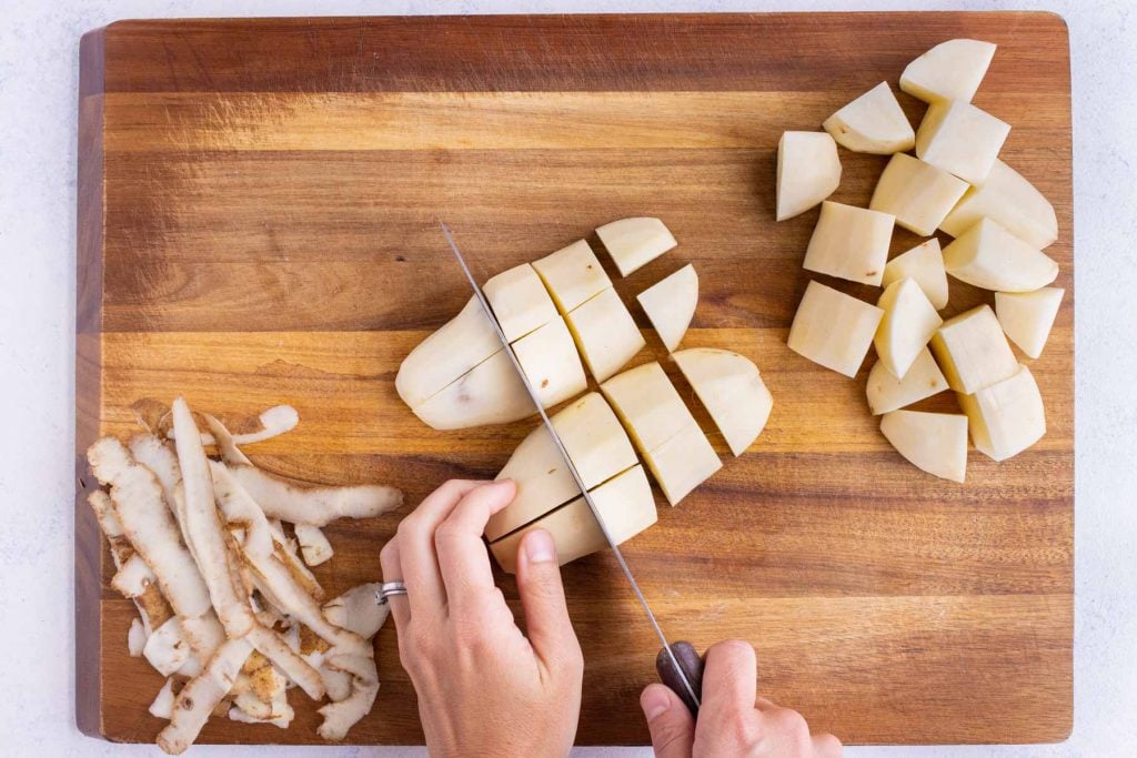 Peeled russet potatoes cut into chunks on a cutting board for pressure cooker potato salad.